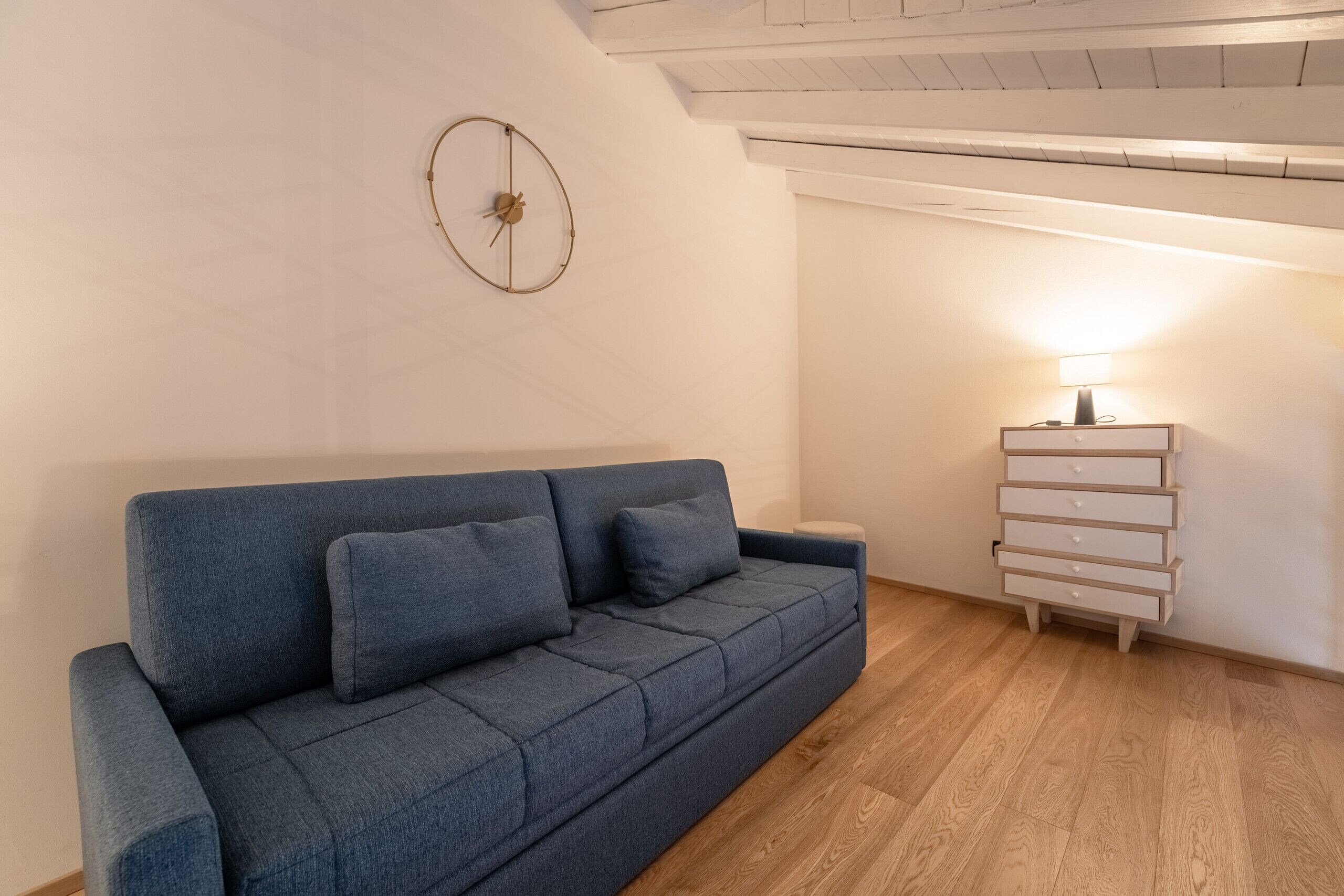 Een moderne woonkamer met een blauwe bank, een houten dressoir en een wandklok.