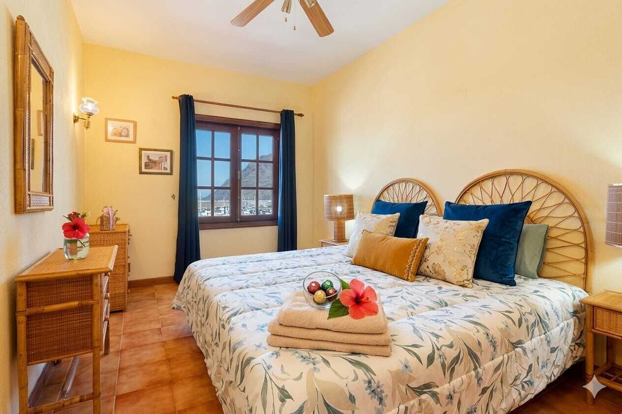 A bedroom with a bed, a bedside table, a lamp, a window with curtains, and a view of the outside.