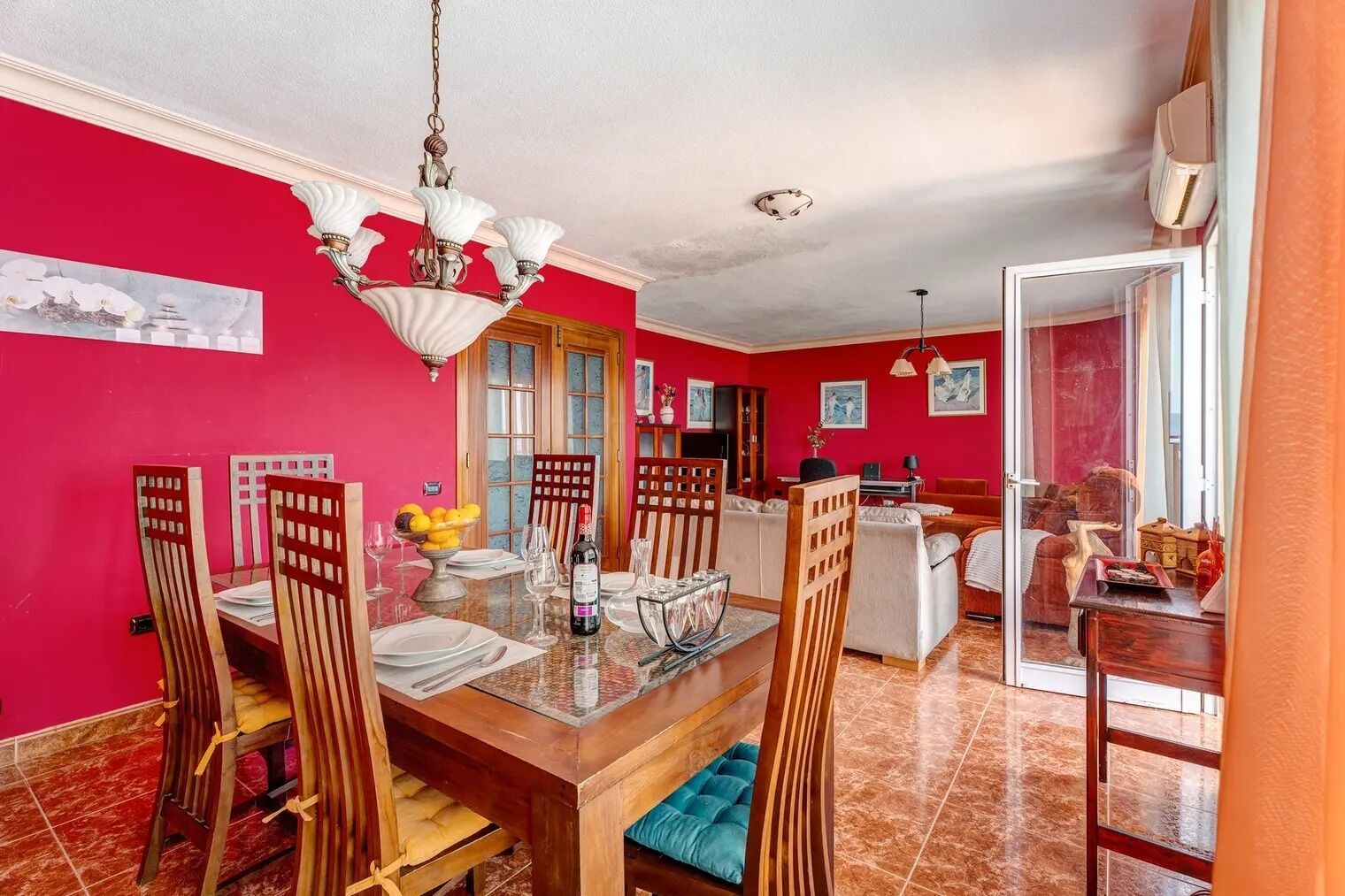 Un coin repas avec une table et des chaises en bois, un lustre et un mur rouge.