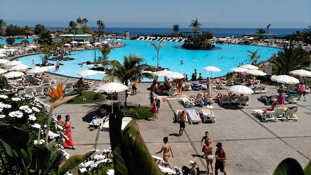 Una grande piscina all'aperto circondata da lettini e ombrelloni, con palme e una vista aperta sull'oceano.