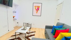 A modern living room with a grey sofa, colorful cushions, a white coffee table, a patterned rug, and a flat-screen TV mounted on the wall. - BetaHouse -3BR -Pool Table -Free Parking -Spacious (Greater Manchester)
