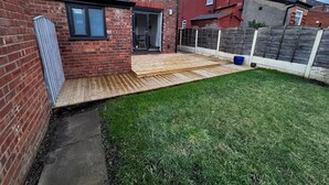 A backyard with a wooden deck, a brick house, and a grassy lawn. - BetaHouse -3BR -Pool Table -Free Parking -Spacious (Greater Manchester)