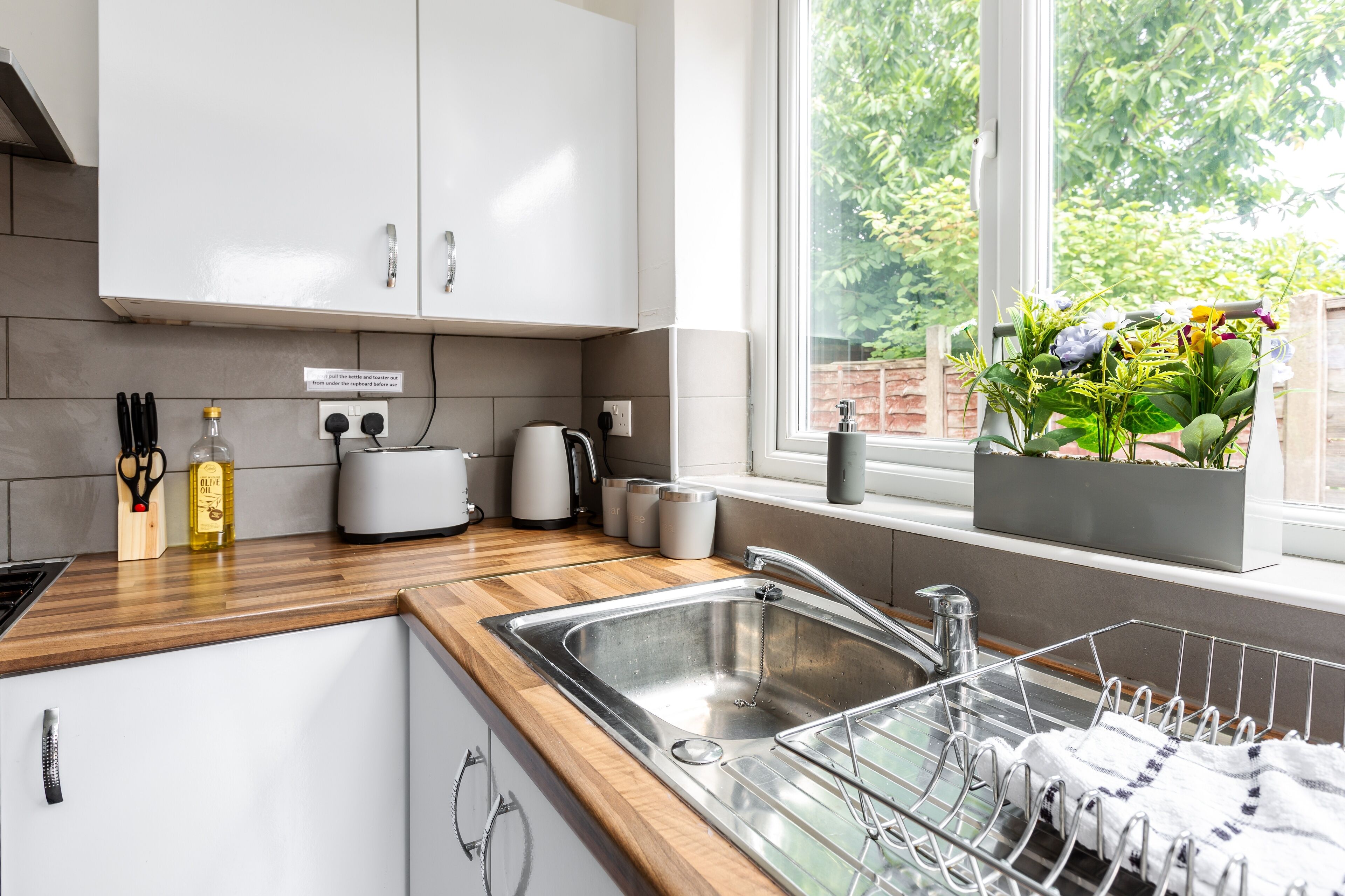 A modern kitchen with a wooden countertop, stainless steel sink, and a window with a view of greenery.
