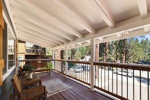 A covered porch with wooden benches, a rug, and a view of a parking lot and trees.