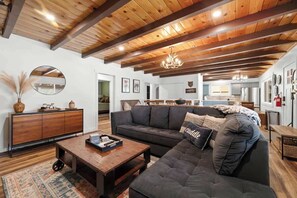 A spacious living room with a dark-colored sectional sofa, a wooden coffee table, and a large mirror on the wall. - RidgeTop Retreat, new rental. (Big Bear Lake)