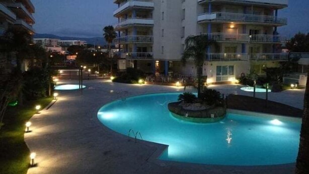 Ein mehrstöckiges Hotel mit Schwimmbad, Außenbeleuchtung und Blick auf die Umgebung.