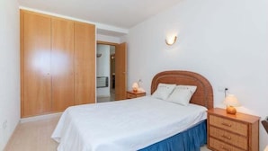 Ein Schlafzimmer mit Bett, Nachttischen, einem Kleiderschrank und einer Wandleuchte.