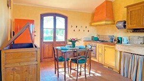 A kitchen with wooden cabinets, a dining table with chairs, a stove, and a window with a view of greenery. - The independent Capannina on the Tuscan hills (Toscana)
