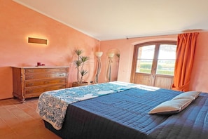 A bedroom with a bed, dresser, potted plants, and a window with curtains.