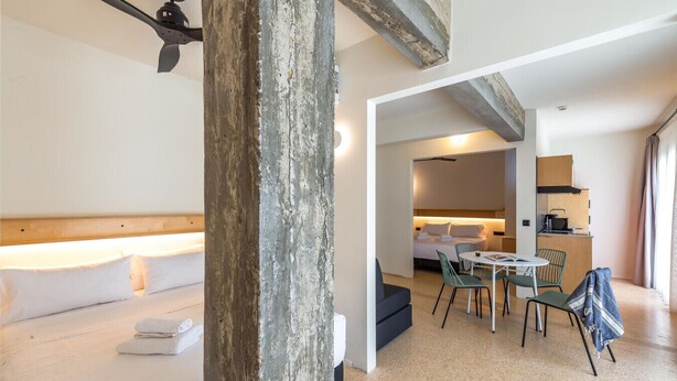 Une chambre d’hôtel comprenant un lit, une table à manger avec des chaises, un coin cuisine et une vue sur l’extérieur.
