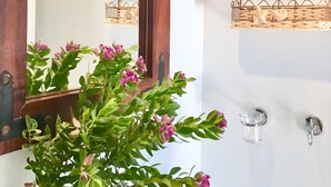 A bathroom with a large mirror, a wooden door, a white sink, and a wall-mounted shelf with decorative items.