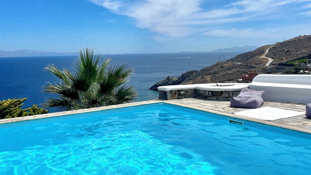 A clear blue swimming pool with a view of the sea and mountains in the background.