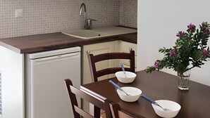 A compact kitchen with white cabinets, a small sink, and a Bosch dishwasher. There is a dining table with two chairs and a vase with flowers.