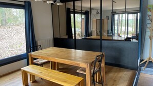 Een eetgedeelte met een houten tafel en banken, grote ramen en uitzicht op de omgeving.