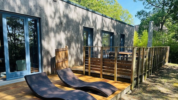 Een modern terras buiten, met twee loungesteunen en een houten dek dat uitloopt vanaf een gebouw met grote ramen.