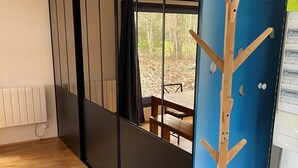 Een kamer met een schuifdeur die uitkomt op een uitzicht over een bos, een houten kapstok en een bank.