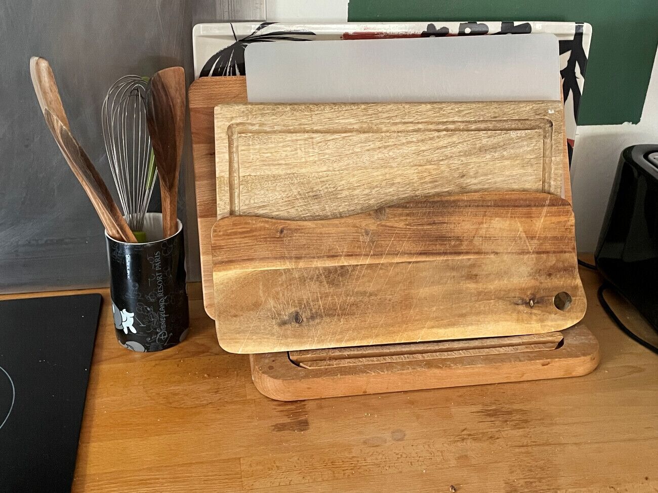 A wooden cutting board on a wooden table with a whisk in a black canister.