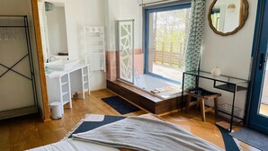 Een moderne slaapkamer met een groot bed, een raam met uitzicht, een kleine badkamer en een balkon met een stoel.