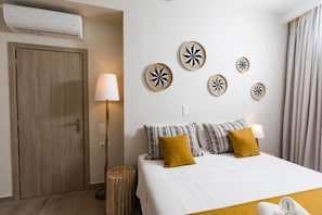 A hotel room with a bed, a wooden door, a lamp, and wall decor.