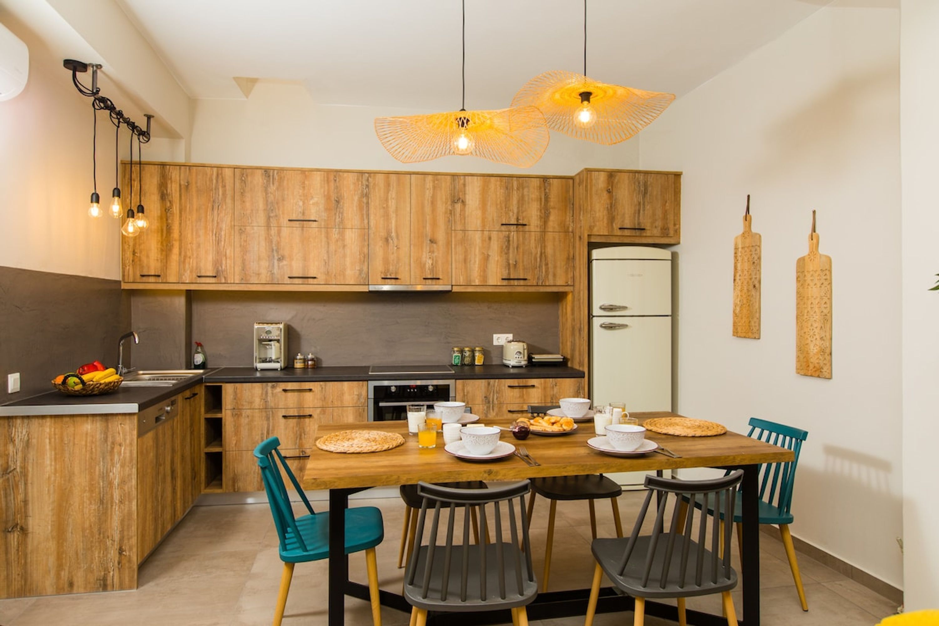 A modern kitchen with wooden cabinets, a dining table with chairs, and pendant lights.
