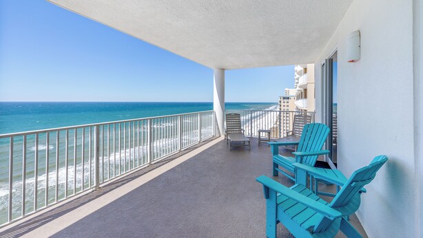 A balcony with a view of the ocean, two blue chairs, and a table.