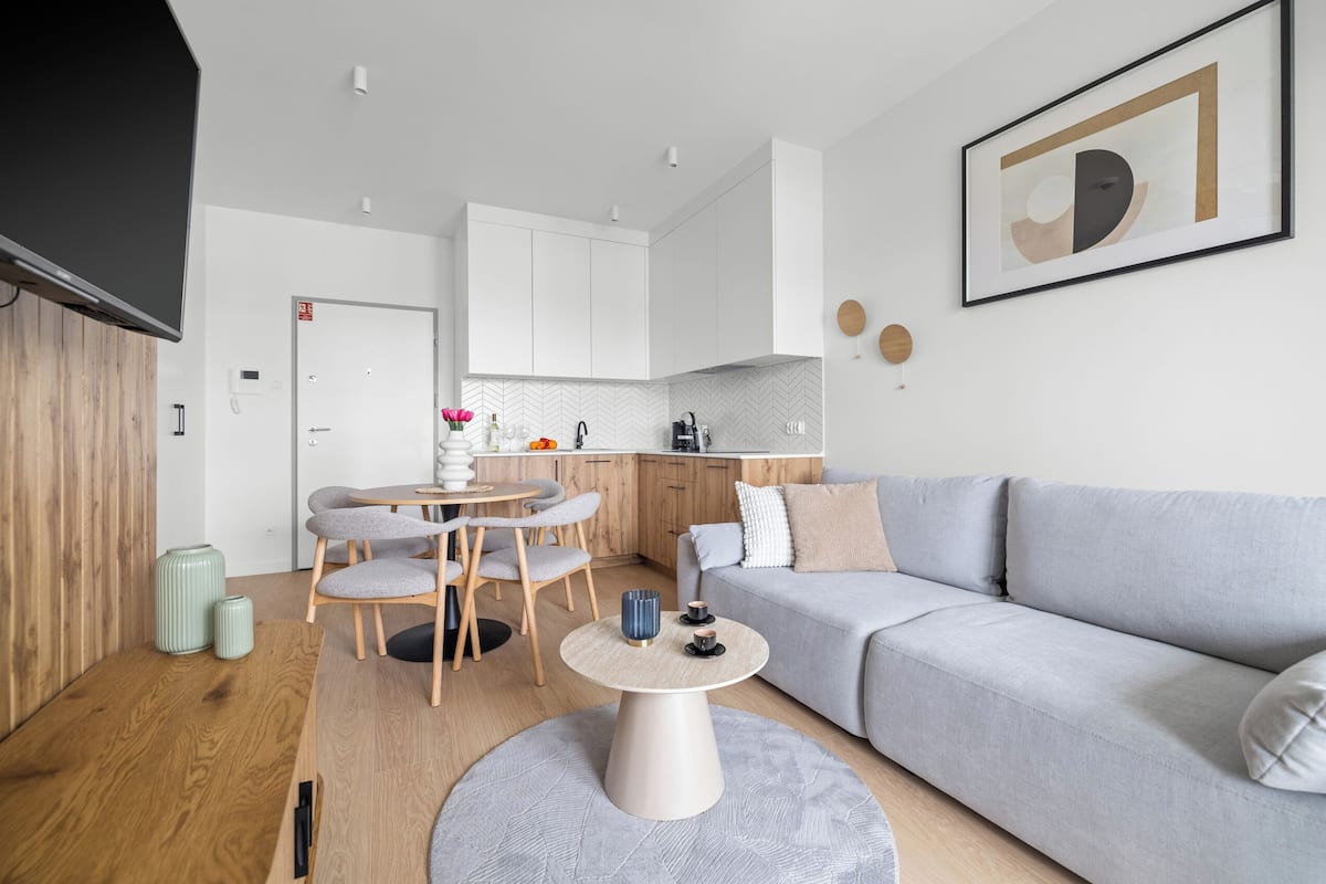 A modern living room with a grey sofa, a round coffee table, and a dining area with a wooden table and chairs.