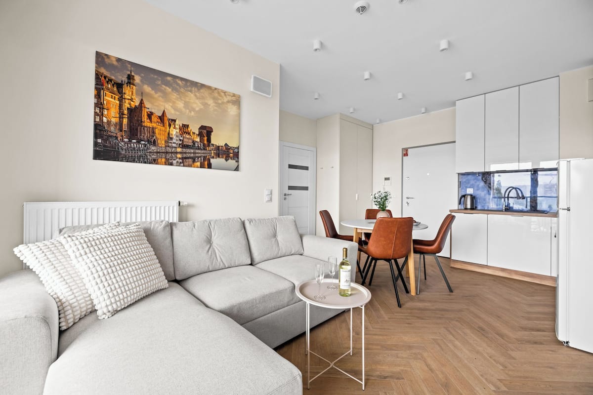 A modern living room with a sofa, a dining table with chairs, and a kitchen area with a refrigerator.