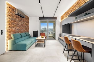Una cocina moderna con horno integrado, una zona de comedor con mesa y sillas, y un amplio ventanal con vistas a un paisaje urbano.