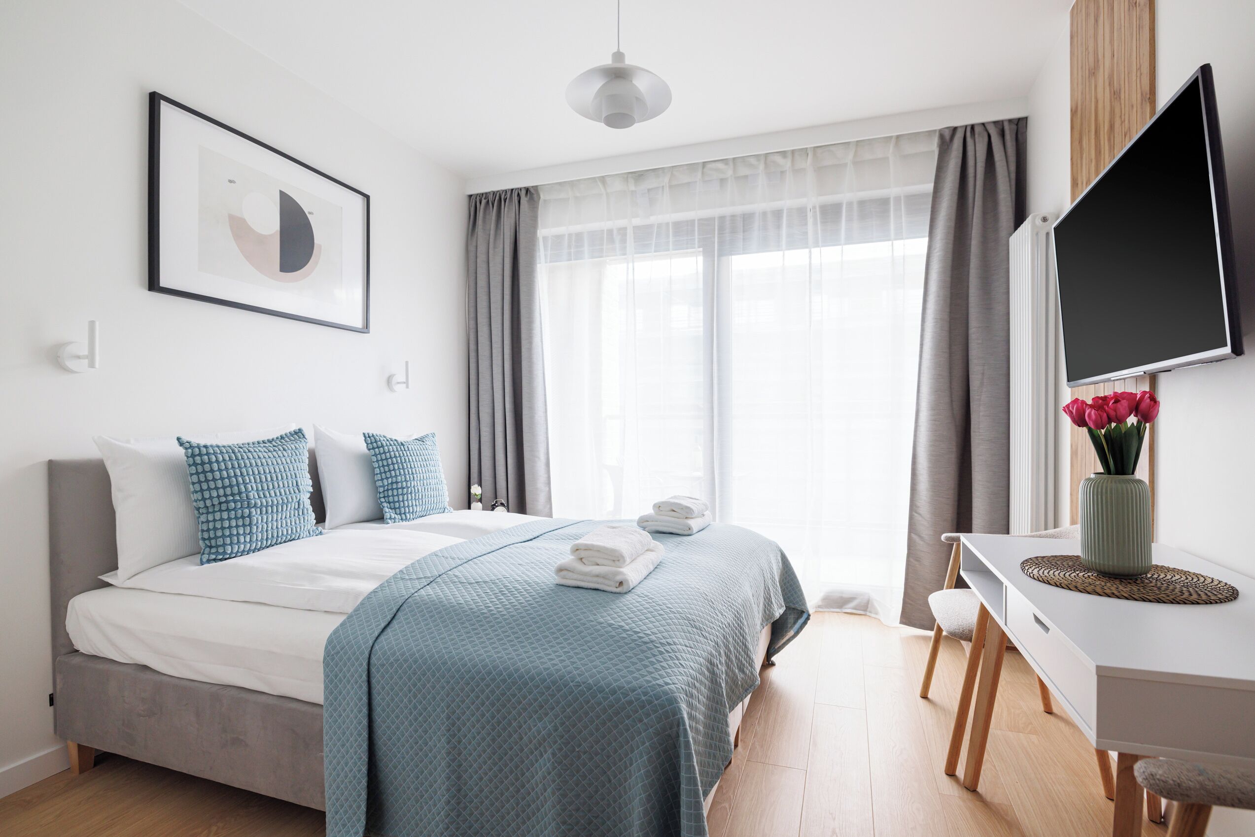 A modern bedroom with a bed, bedside table, TV, and a window with curtains.