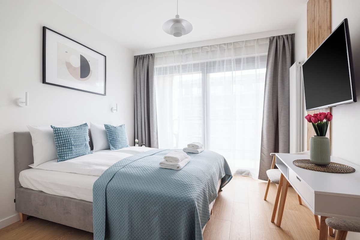 A modern bedroom with a bed, bedside table, TV, and a window with curtains.