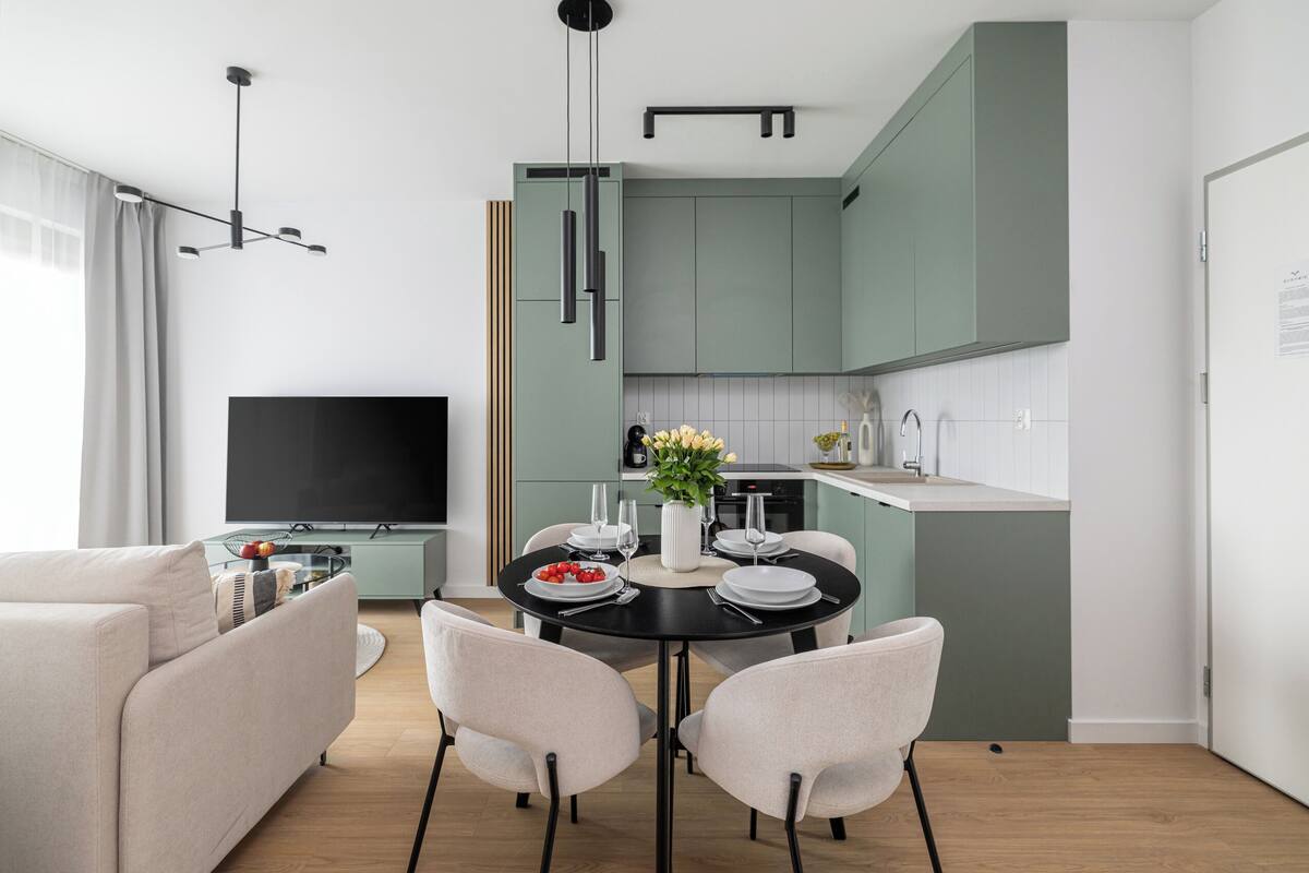 A modern living room with a sofa, dining table, and chairs, a flat-screen TV, and a kitchen area with cabinets and a countertop.