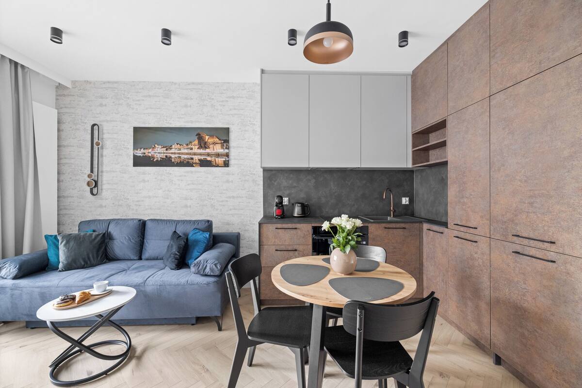 A modern living room with a grey sofa, a round wooden dining table, and black chairs.