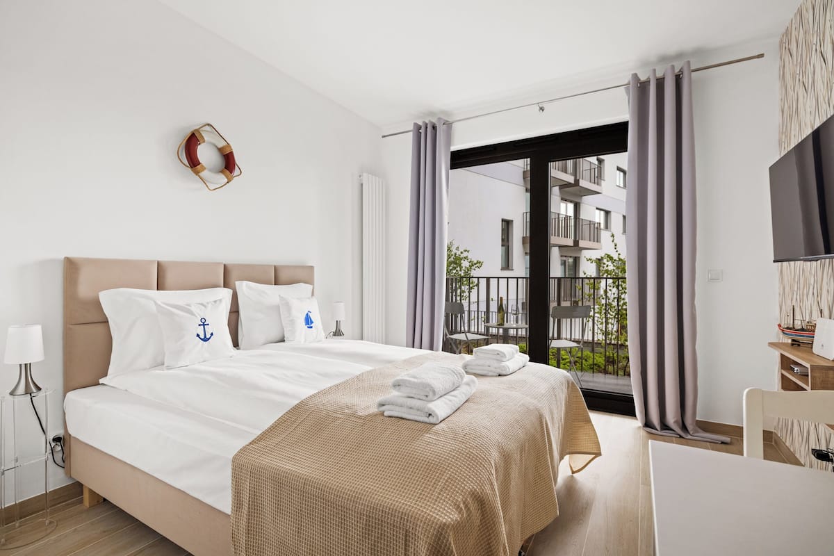 A modern hotel room with a large bed, a flat-screen TV, and a balcony with a view of the city.