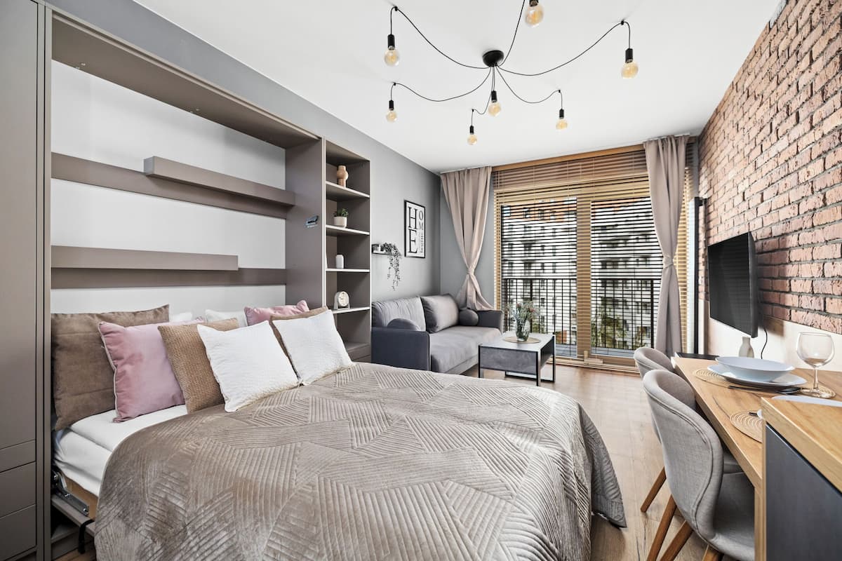 A modern bedroom with a large bed, built-in shelving, a desk, and a TV.