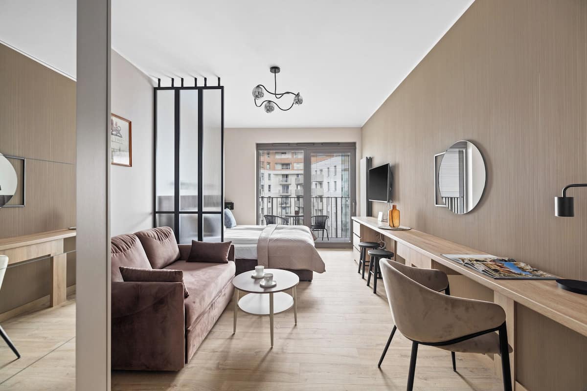 A modern hotel room with a sofa, a bed, a dining area, and a balcony with a city view.