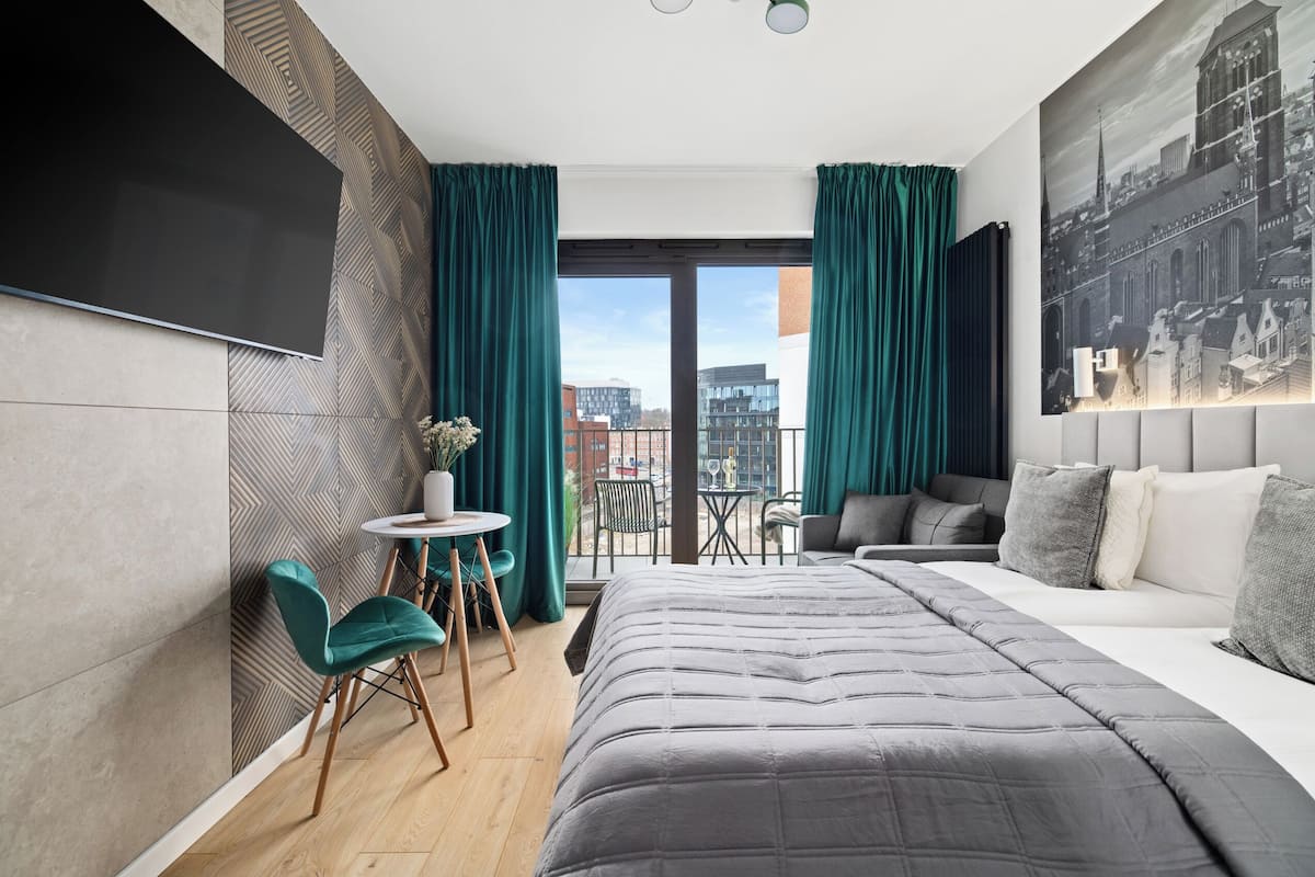 A modern hotel room with a large bed, a flat-screen TV, a small dining area, and a city view.
