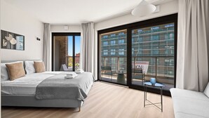 A modern bedroom with a large bed, a sofa, a small table, and a view of a cityscape through a large window. - City Break Żurawie Aparthotel  (Gdansk)