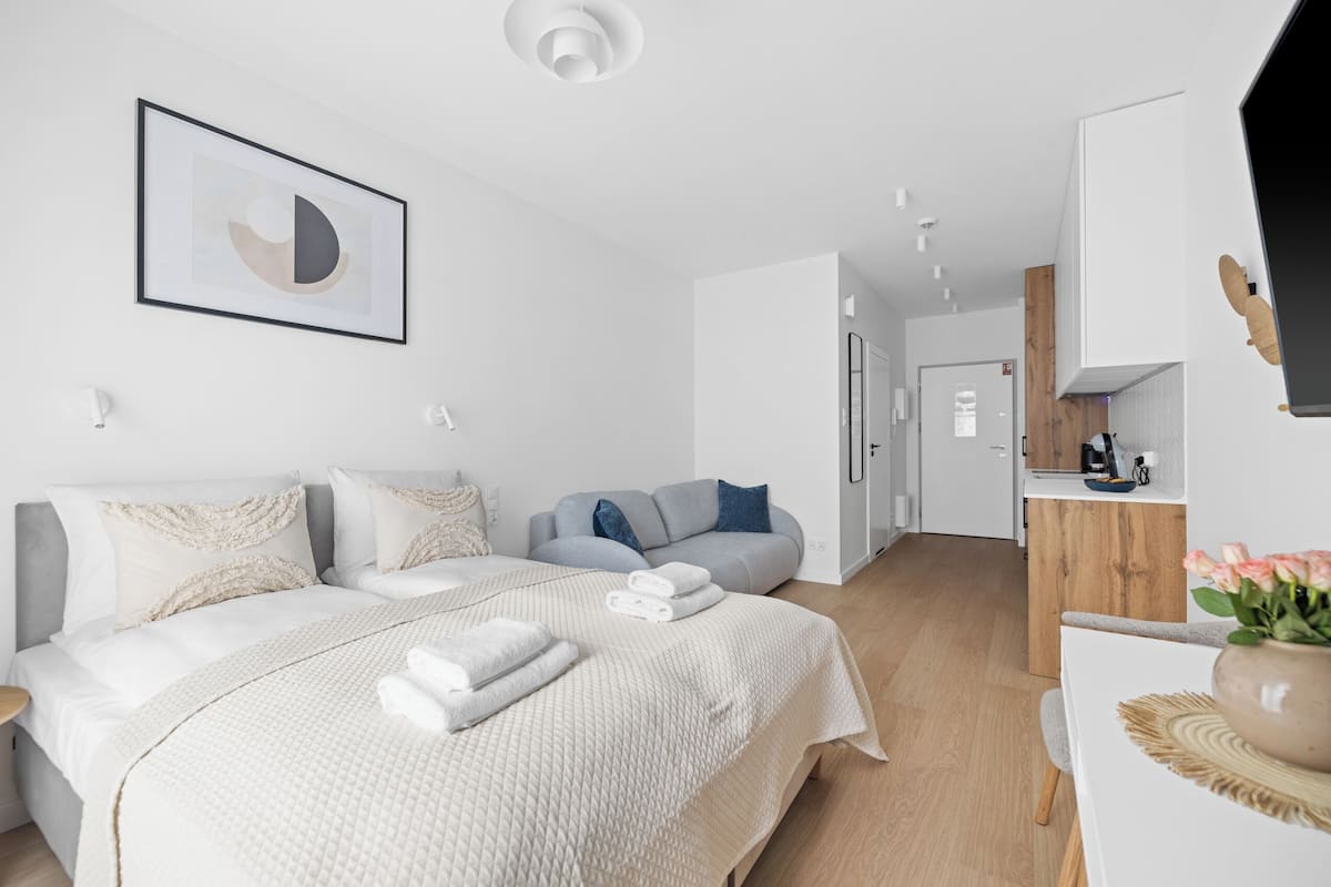 A modern hotel room with a large bed, a sofa, a wooden cabinet, and a framed artwork on the wall.
