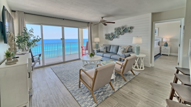 Un vaste espace de vie avec balcon, ventilateur de plafond et ensemble de canapés.