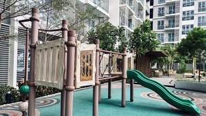 A playground with a slide and climbing structures, surrounded by a patterned carpet and greenery, with a modern building in the background. - Peaceful & Private Hideout (Iloilo)