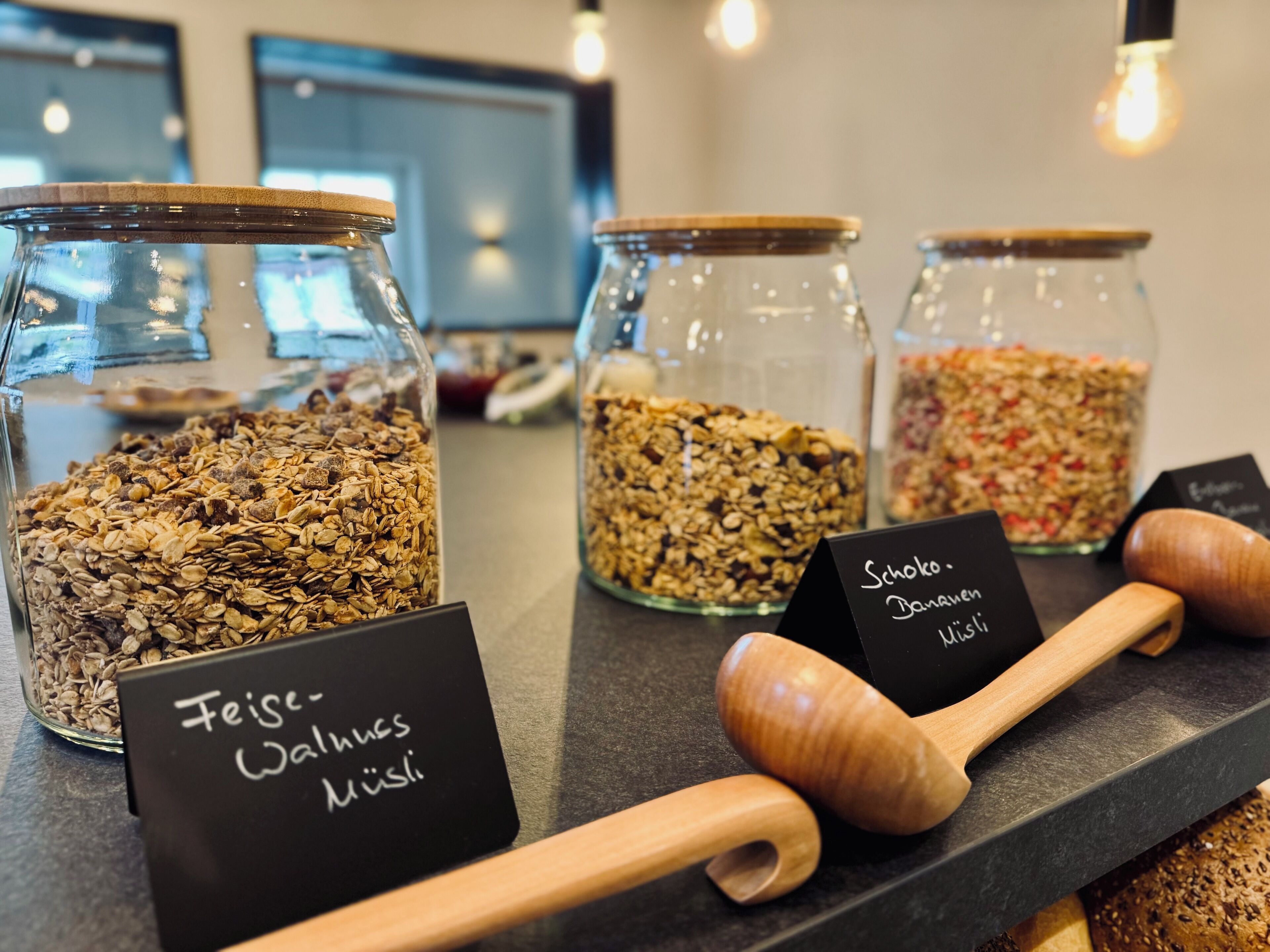 Tres frascos de vidrio llenos de diferentes tipos de granola sobre una encimera, cada uno con un nombre.