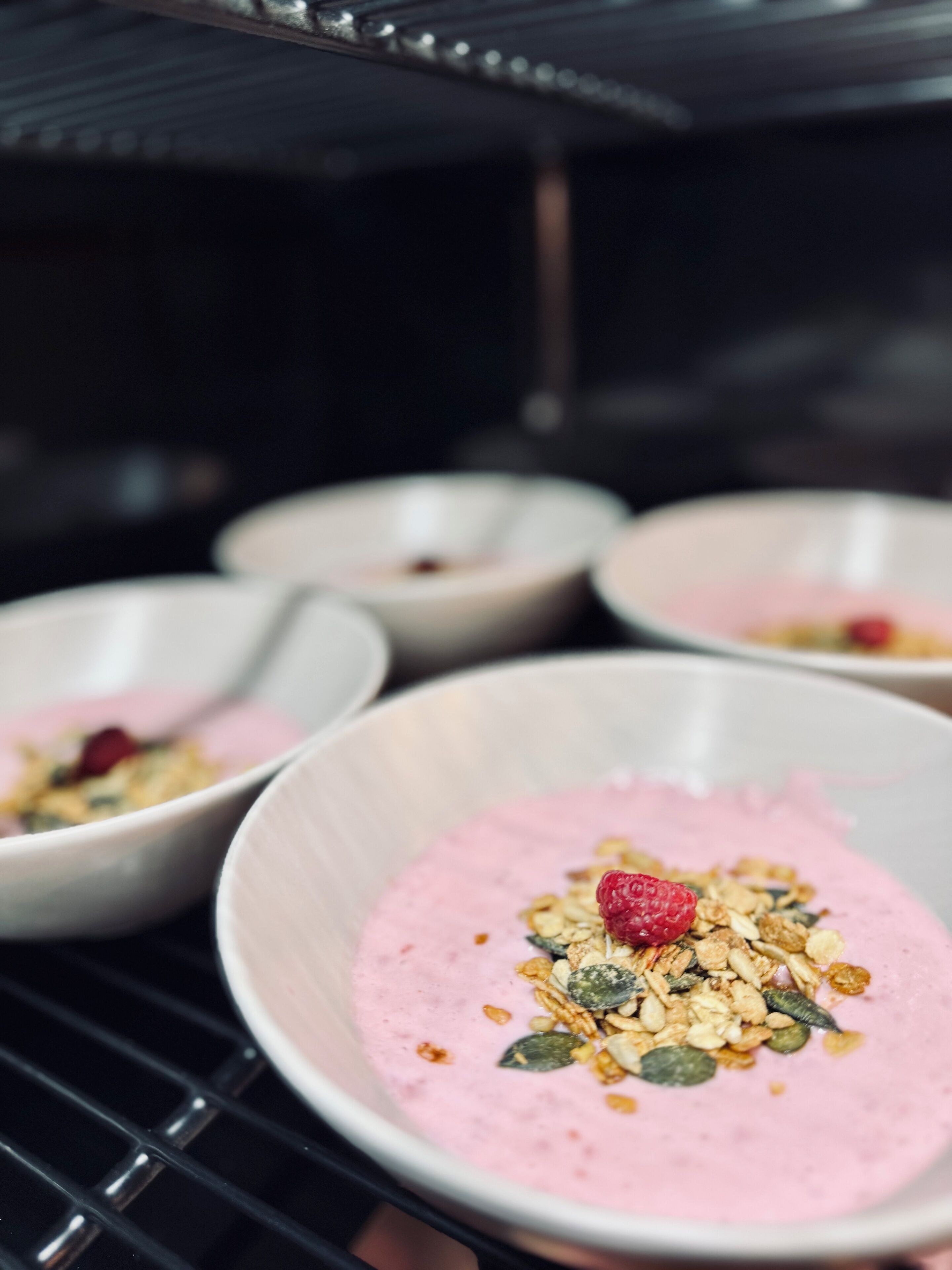 Ein Nahaufnahme von einem Dessert mit rosa Belag, verziert mit Samen und einer Himbeere, serviert in einer Schüssel.