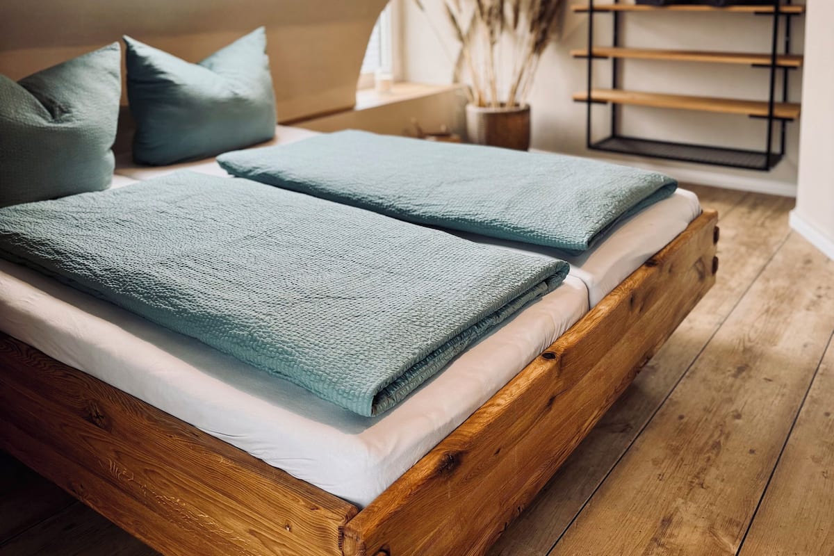 A loft bedroom with a sloped ceiling, a skylight, a wooden bed frame, and a built-in shelf with towels.