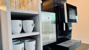 A coffee machine with a digital display and a shelf with white cups and glass bottles.