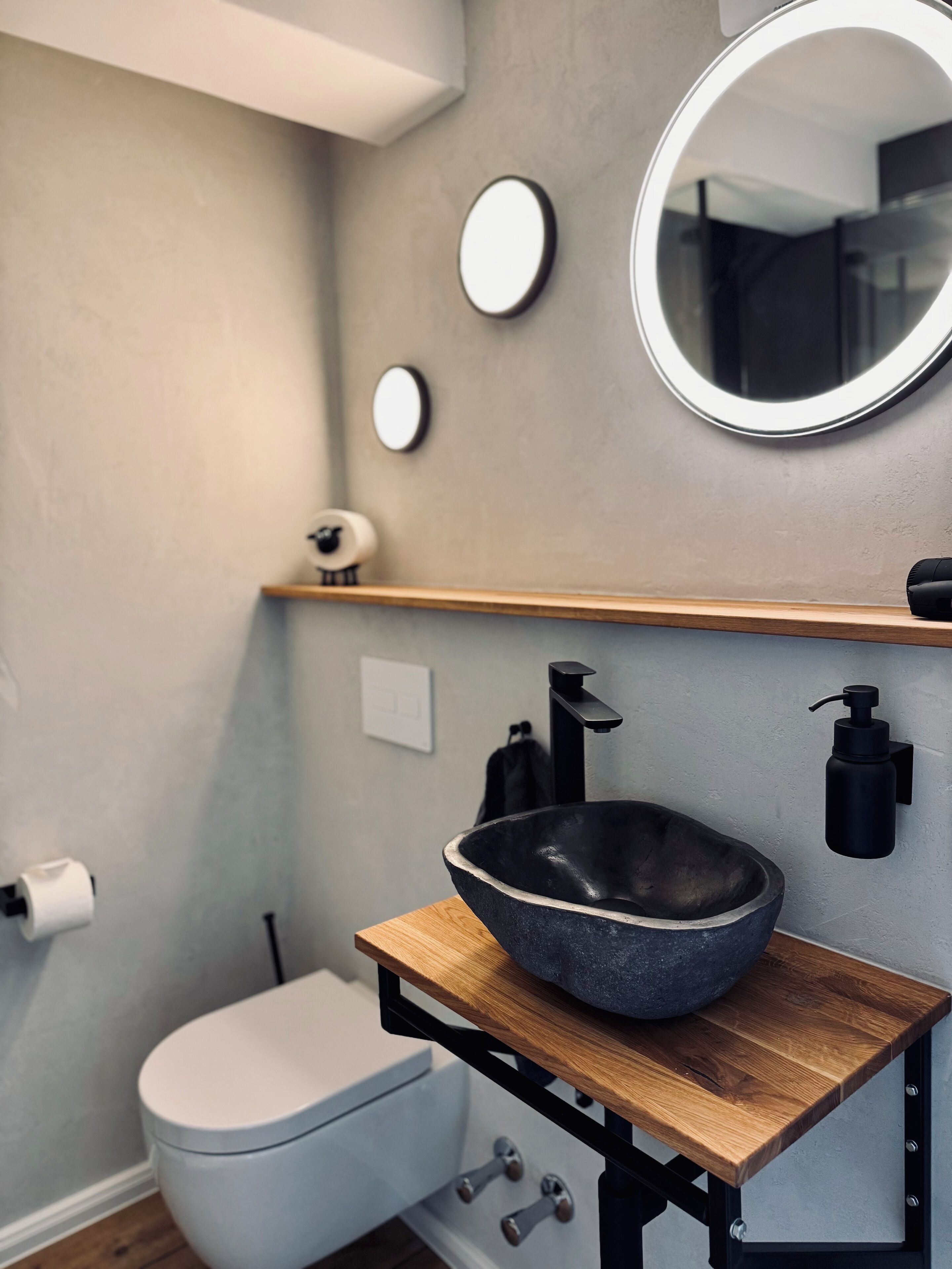 A modern bathroom with a stone sink, a toilet, and a mirror.
