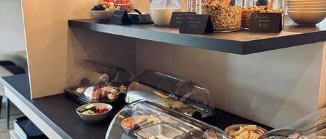 Um buffet de café da manhã com diversos alimentos e recipientes, incluindo frutas, cereais e laticínios.