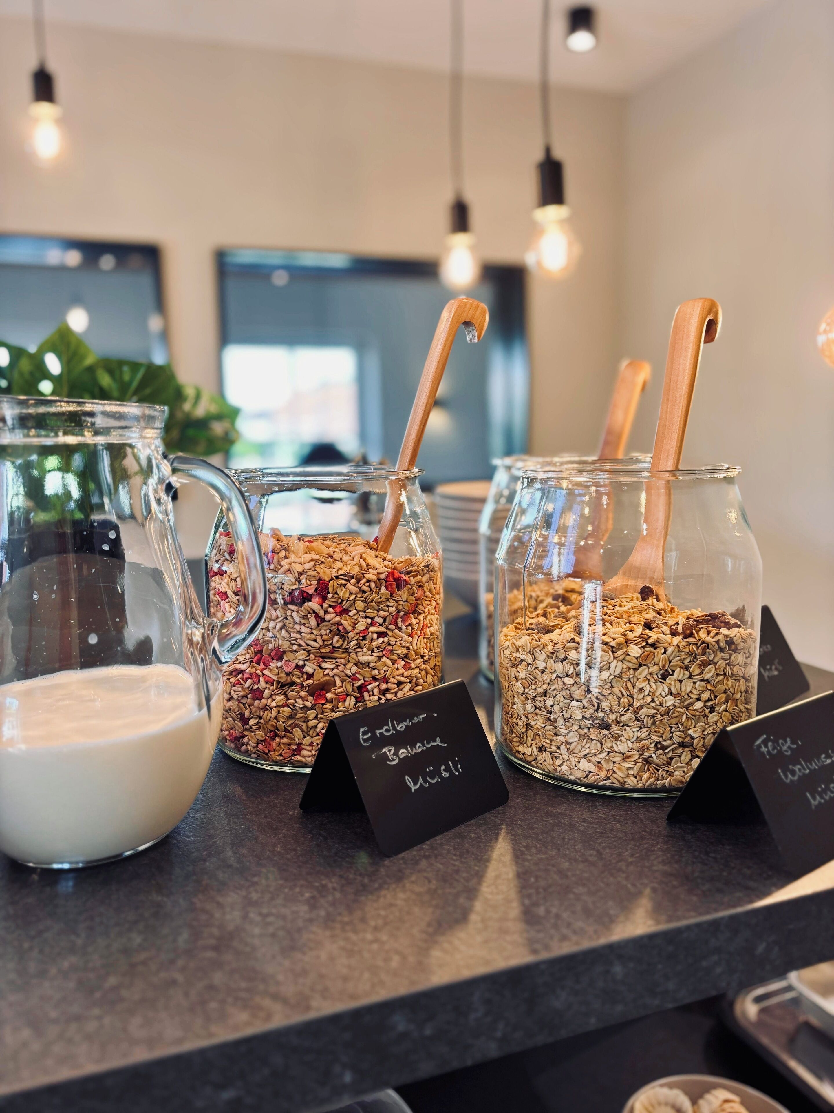 Een presentatie van voedsel met diverse potten granola en een kan melk, elk voorzien van verschillende namen.