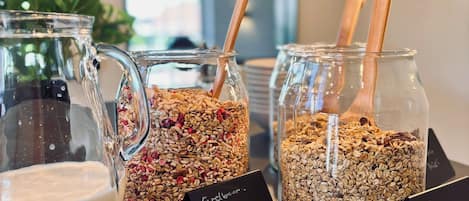Una presentación de comida con varios tarros de granola y una jarra de leche, cada uno etiquetado con nombres distintos.