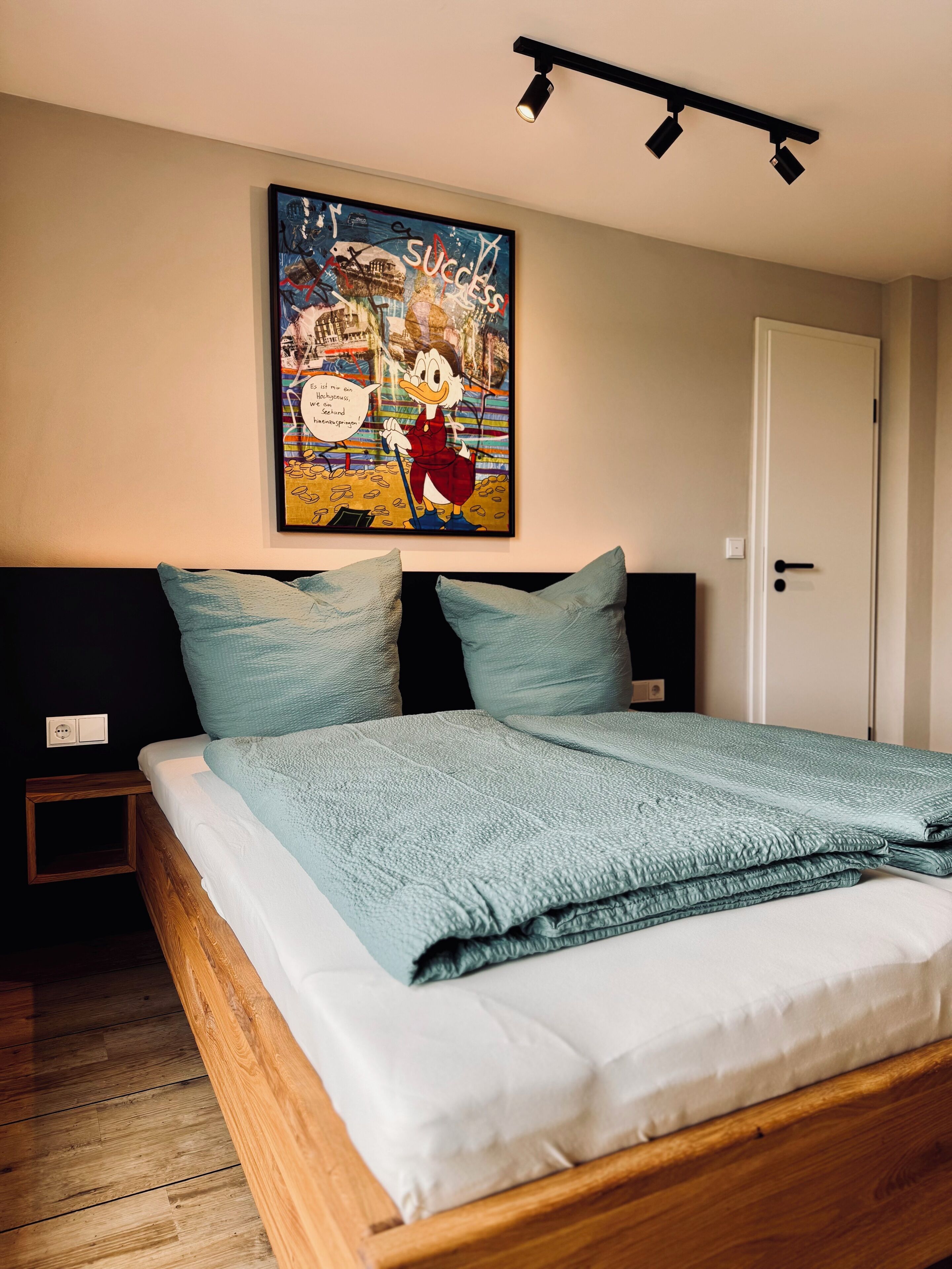 A bedroom with a bed, a painting on the wall, and a door.