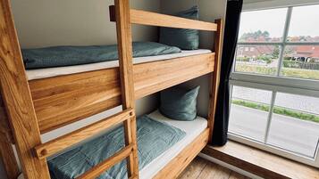 A bunk bed with a wooden ladder, a window with a view of houses, and a ceiling light fixture.